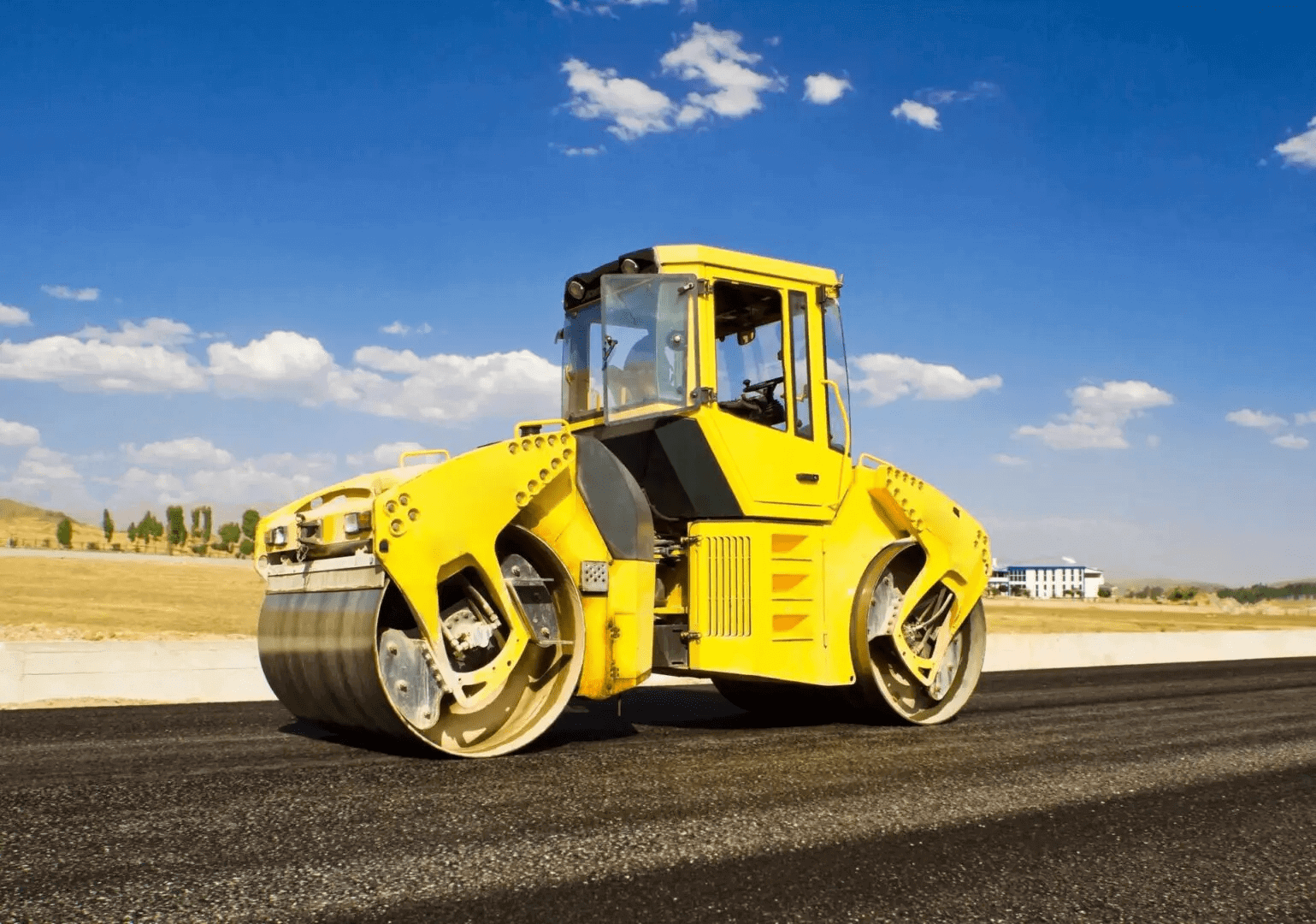 Bright yellow road roller compacting asphalt on a sunny day.